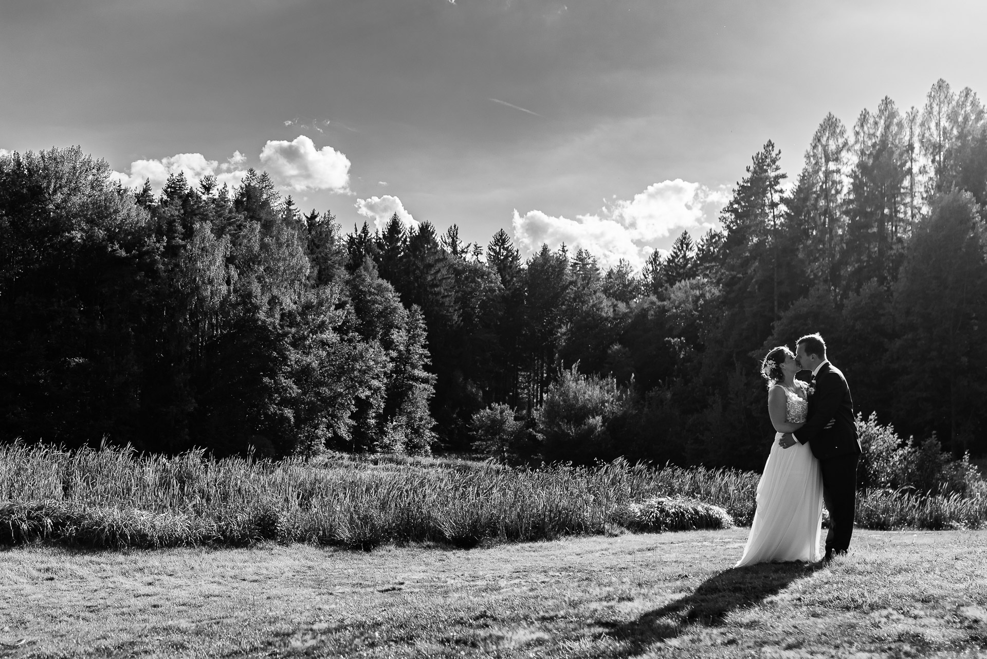 Černobílá svatební fotografie nevěsty a ženicha v objetí uprostřed přírodní scenérie.